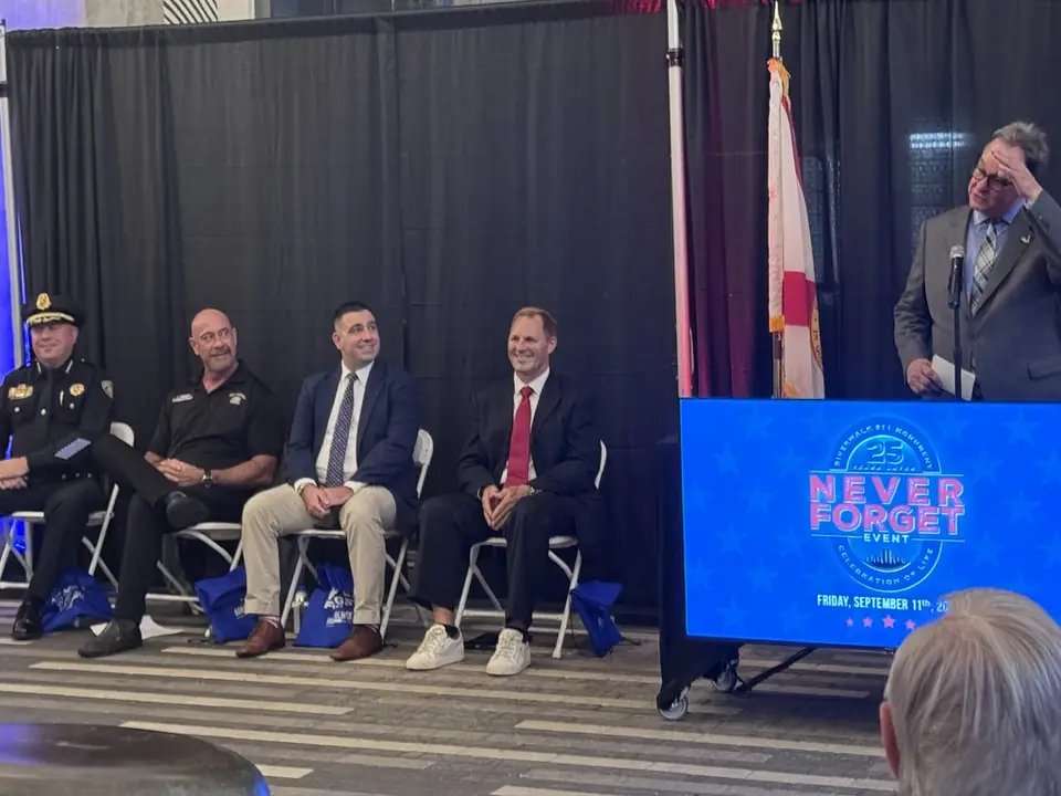 Uniformed and civilian guests seated on stage as a speaker talks.