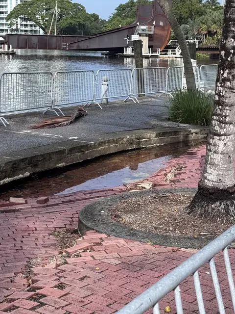 The barricaded walkway west of Andrews Avenue, showing displaced pavers and standing water behind the seawall cap.
